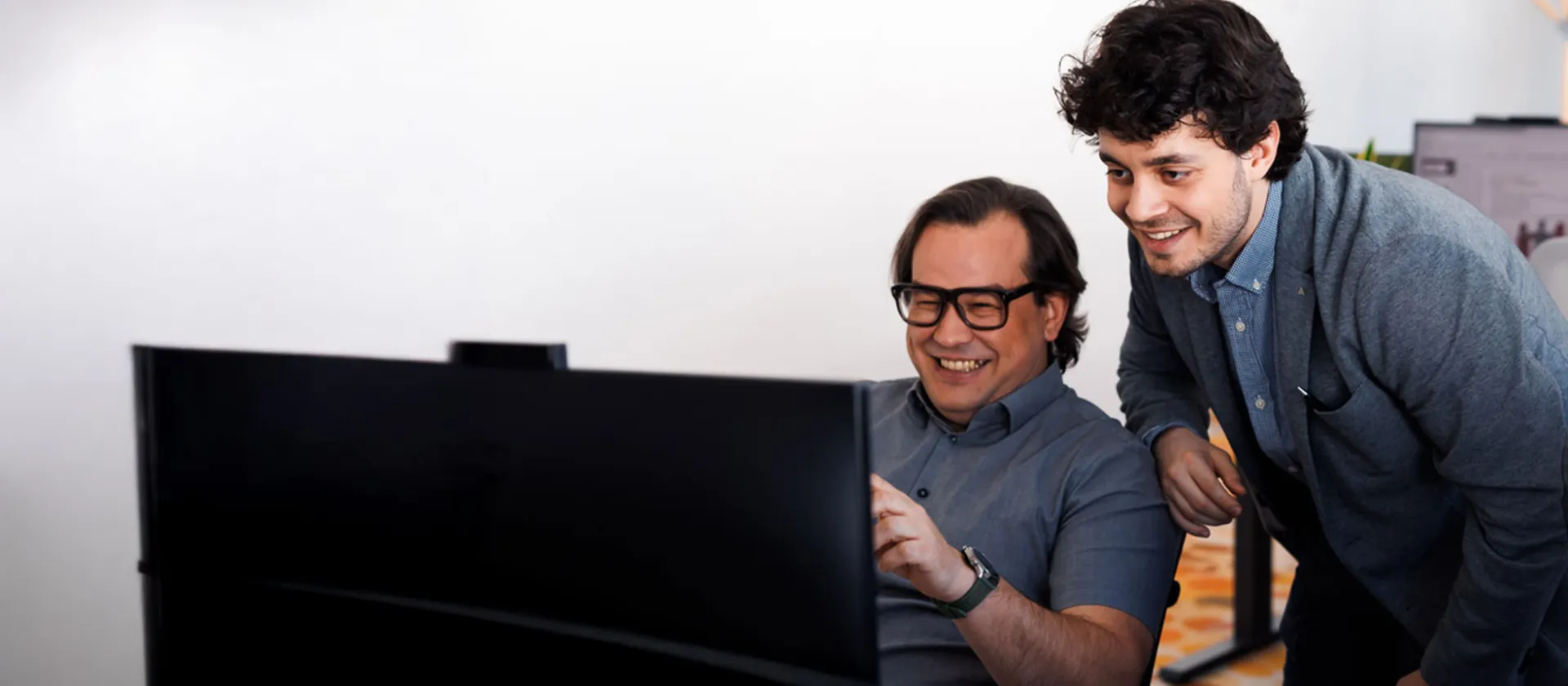 Two colleagues collaborating in front of a computer screen, smiling and discussing project details in a modern office environment.