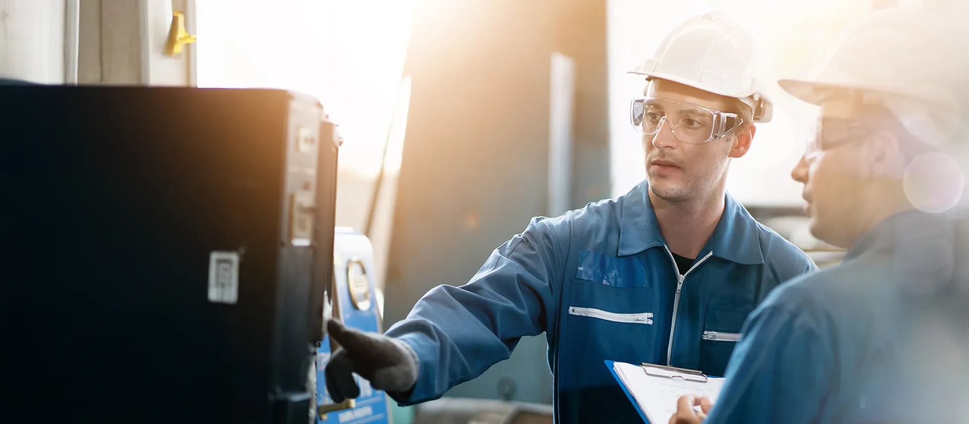 Two engineers in safety gear inspecting industrial equipment in a discrete manufacturing facility, focusing on process reliability and operational efficiency.
