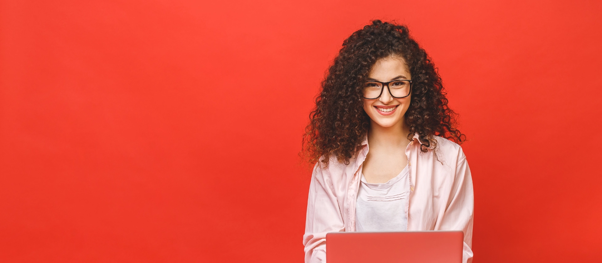 junge Auszubildende oder Schülerin im Schneidersitz mit Laptop vor rotem Hintergrund