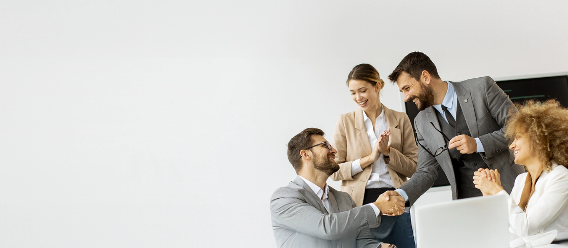 Dynamische Business-Szene: Zwei Männer begrüßen sich mit einem Händedruck, während zwei Kolleginnen lächelnd applaudieren 