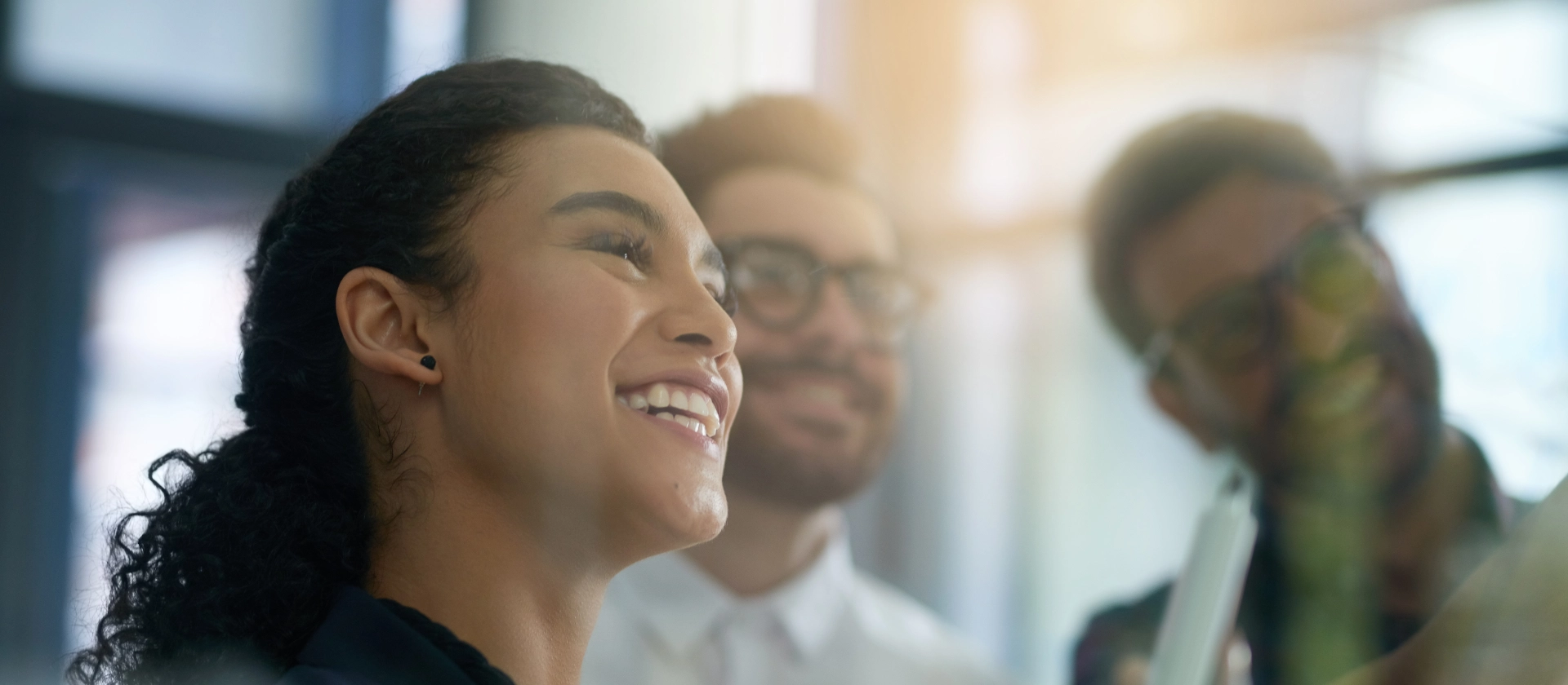 Eine Frau und zwei Männer im Office lächelnd