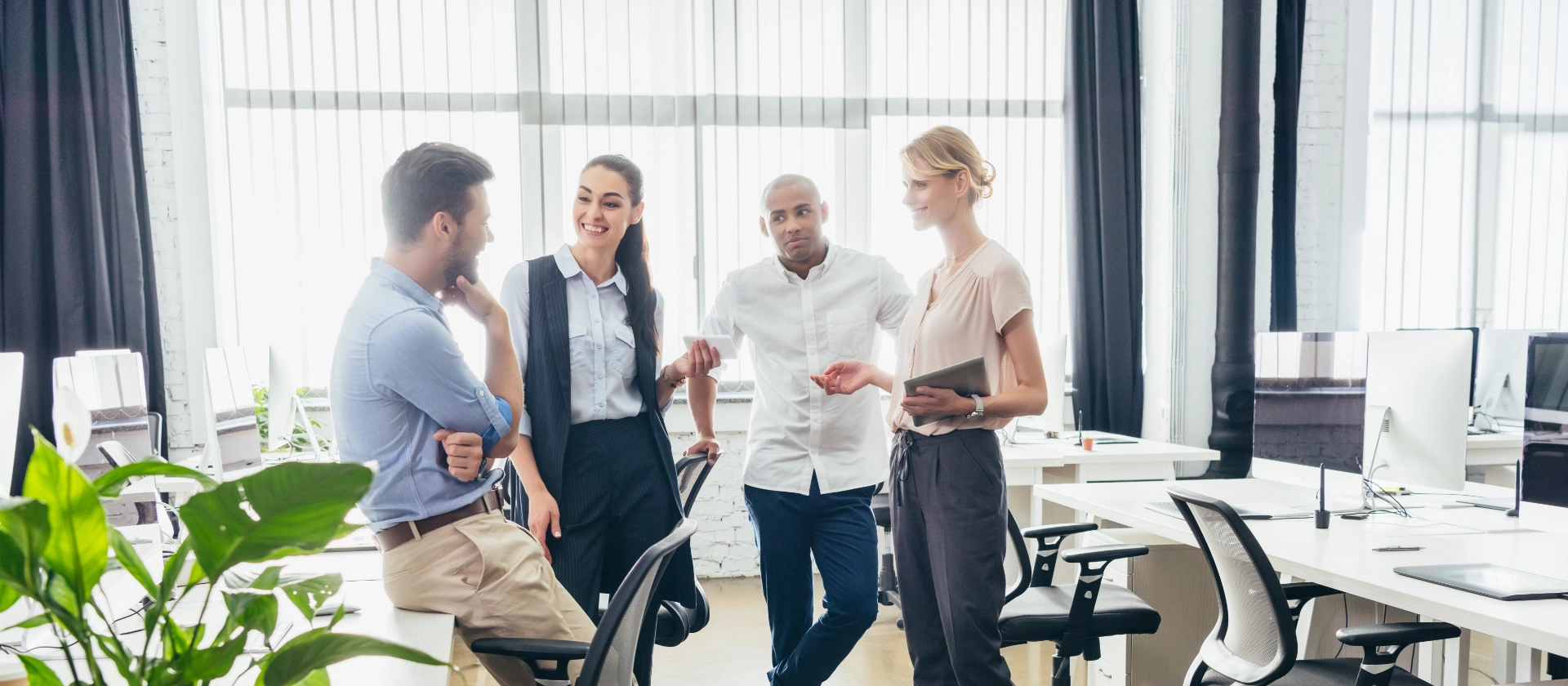 Zwei Männer und zwei Frauen stehen in einem hellen Großraumbüro zusammen und unterhalten sich