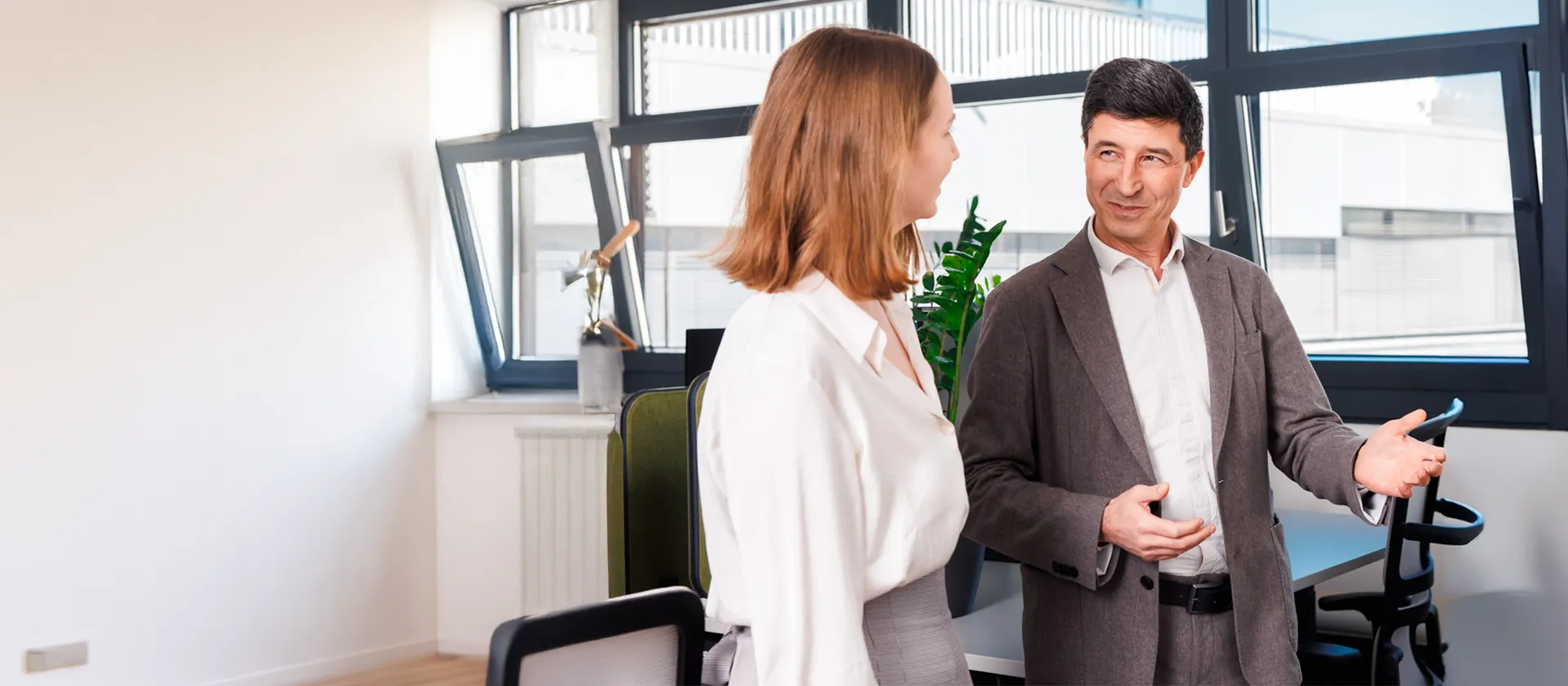 Businesswoman and businessman in a modern office space engaged in a professional conversation, symbolizing collaboration and consulting in a digital business environment.