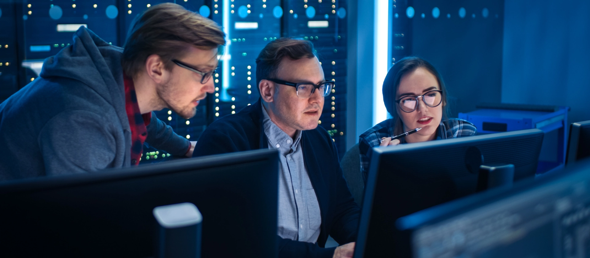 Zwei Kollegen und eine Kollegin aus dem Bereich Cyber Security sitzen konzentriert an einem Arbeitsplatz vor ihren Rechnern