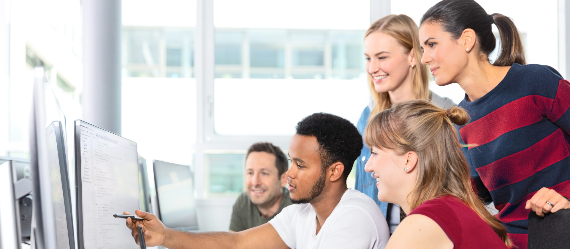 Eine gemischte Gruppe msg-Mitarbeitender kommt an einem Arbeitsplatz zusammen, um ein Arbeitsergebnis anzusehen