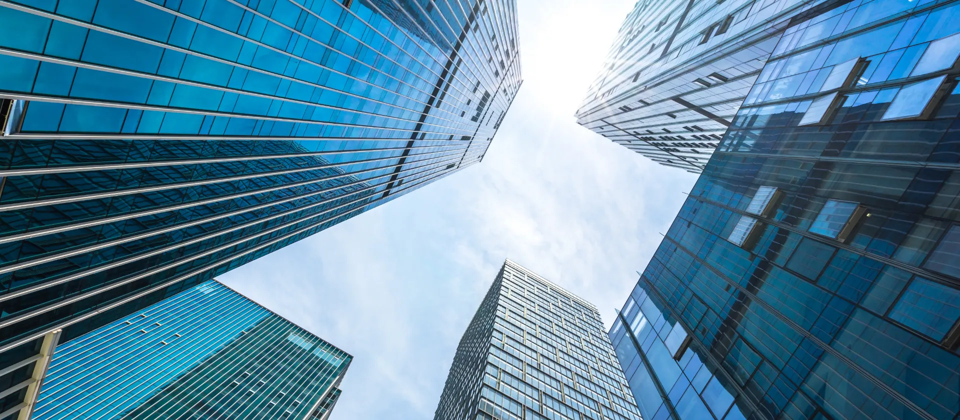 View looking up at modern glass skyscrapers against a bright sky, symbolizing innovation, growth, and corporate vision.