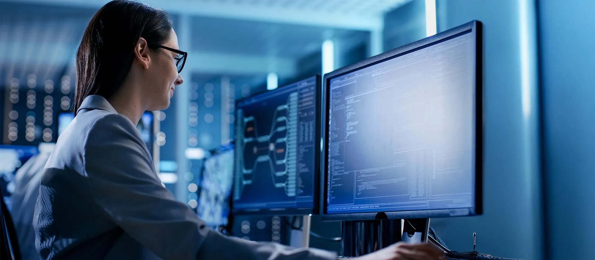 Female IT specialist analyzing data on dual monitors in a secure, high-tech operations center, representing cybersecurity, system monitoring, and enterprise technology.