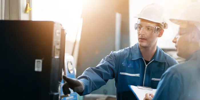 Two engineers in safety gear inspecting industrial equipment in a discrete manufacturing facility, focusing on process reliability and operational efficiency.