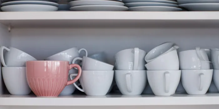  Close-up of white coffee cups stacked on a shelf with one standout pink cup, symbolizing individuality and innovation.