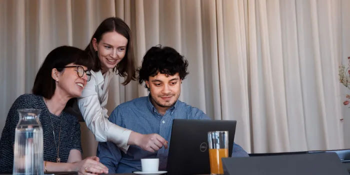 Three msg Plaut team members collaborating at a laptop, discussing digital transformation strategies in a relaxed and engaging meeting environment.