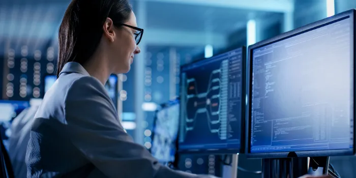 Female IT specialist analyzing data on dual monitors in a secure, high-tech operations center, representing cybersecurity, system monitoring, and enterprise technology.