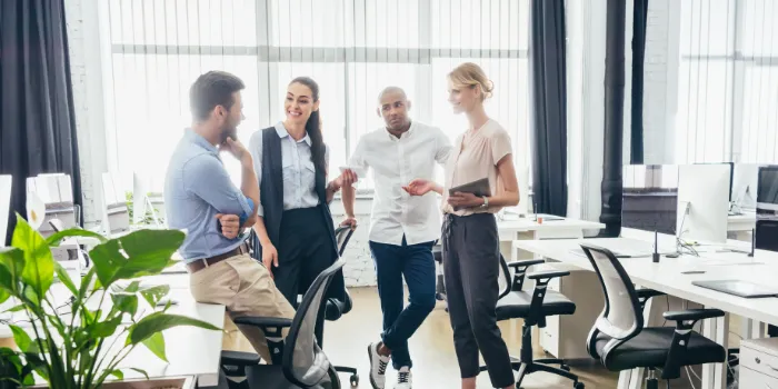 Zwei Männer und zwei Frauen stehen in einem hellen Großraumbüro zusammen und unterhalten sich