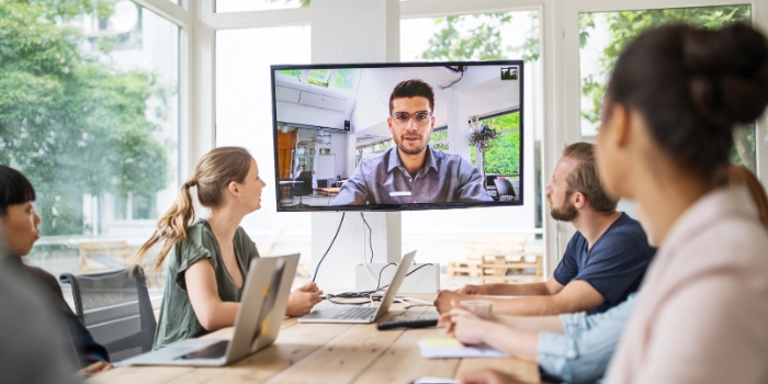 Eine gemischte Gruppe Mitarbeitender der Branche Banking unterhalten sich in einem Remote Meeting mit einem Kollegen, der via Bildschirm zugeschaltet ist