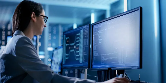 Female IT specialist analyzing data on dual monitors in a secure, high-tech operations center, representing cybersecurity, system monitoring, and enterprise technology.