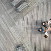 Aerial view of a diverse business team standing in a circle on a wooden deck, joining hands in the center to symbolize collaboration, innovation, and shared goals.