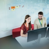 Männlicher und weibliche IT Consultant von oben an ihrem Arbeitsplatz neben einem Whiteboard