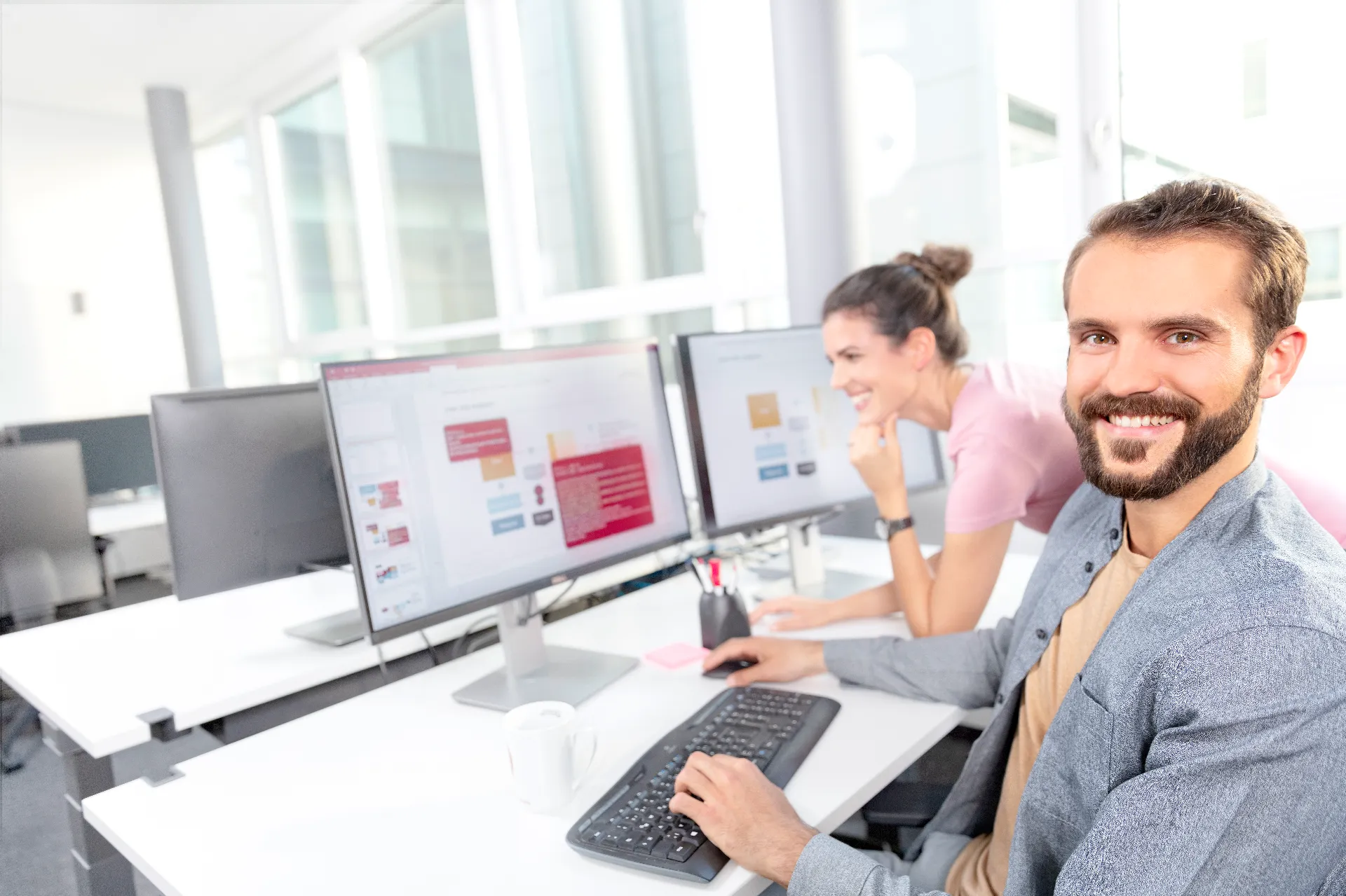 Zwei erfahrene Mitarbeitenden nebeneinander sitzend an ihren Arbeitsplätzen