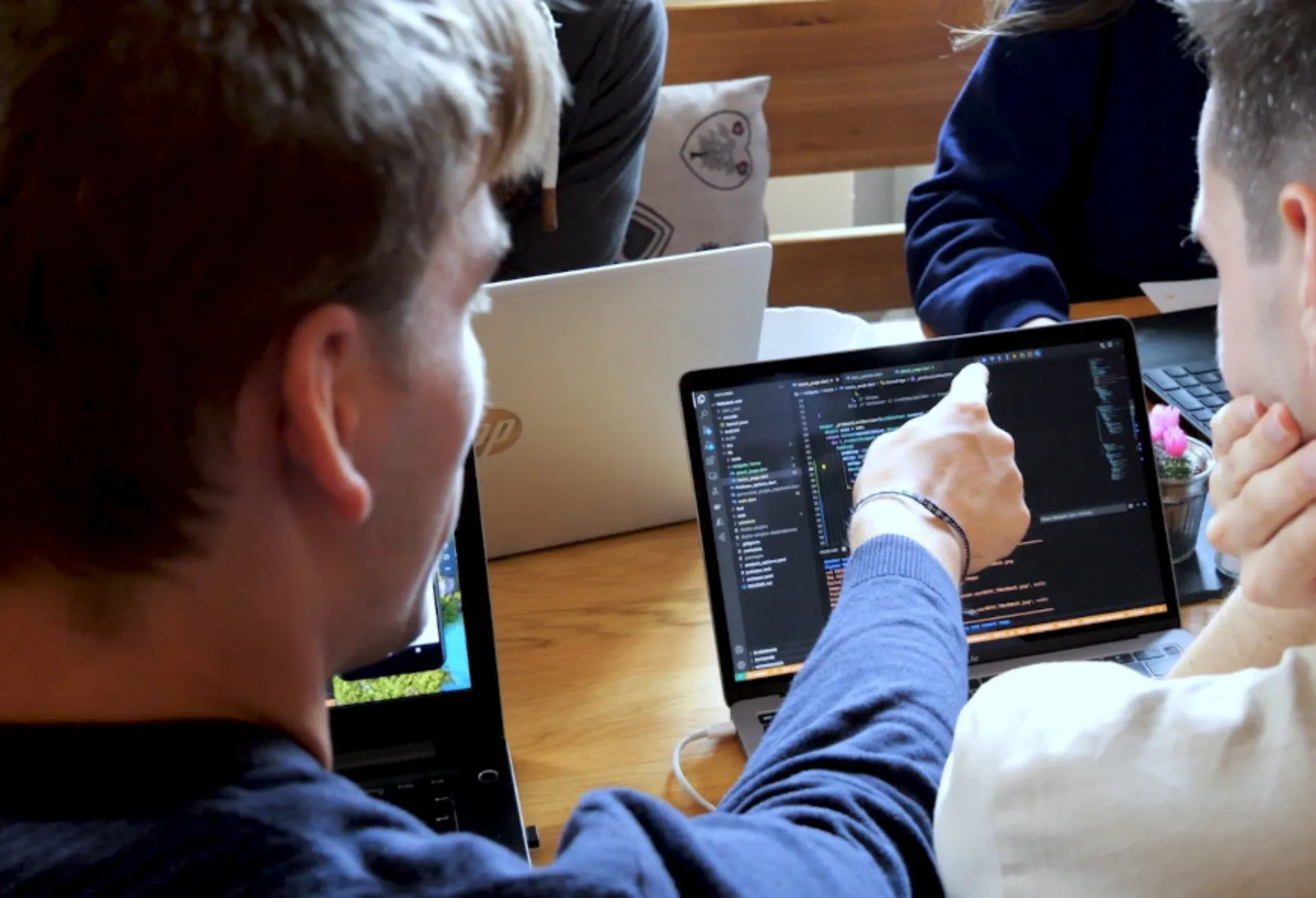 Studierende beratschlagen vor einem Laptop mit Code-Zeilen auf dem Bildschirm