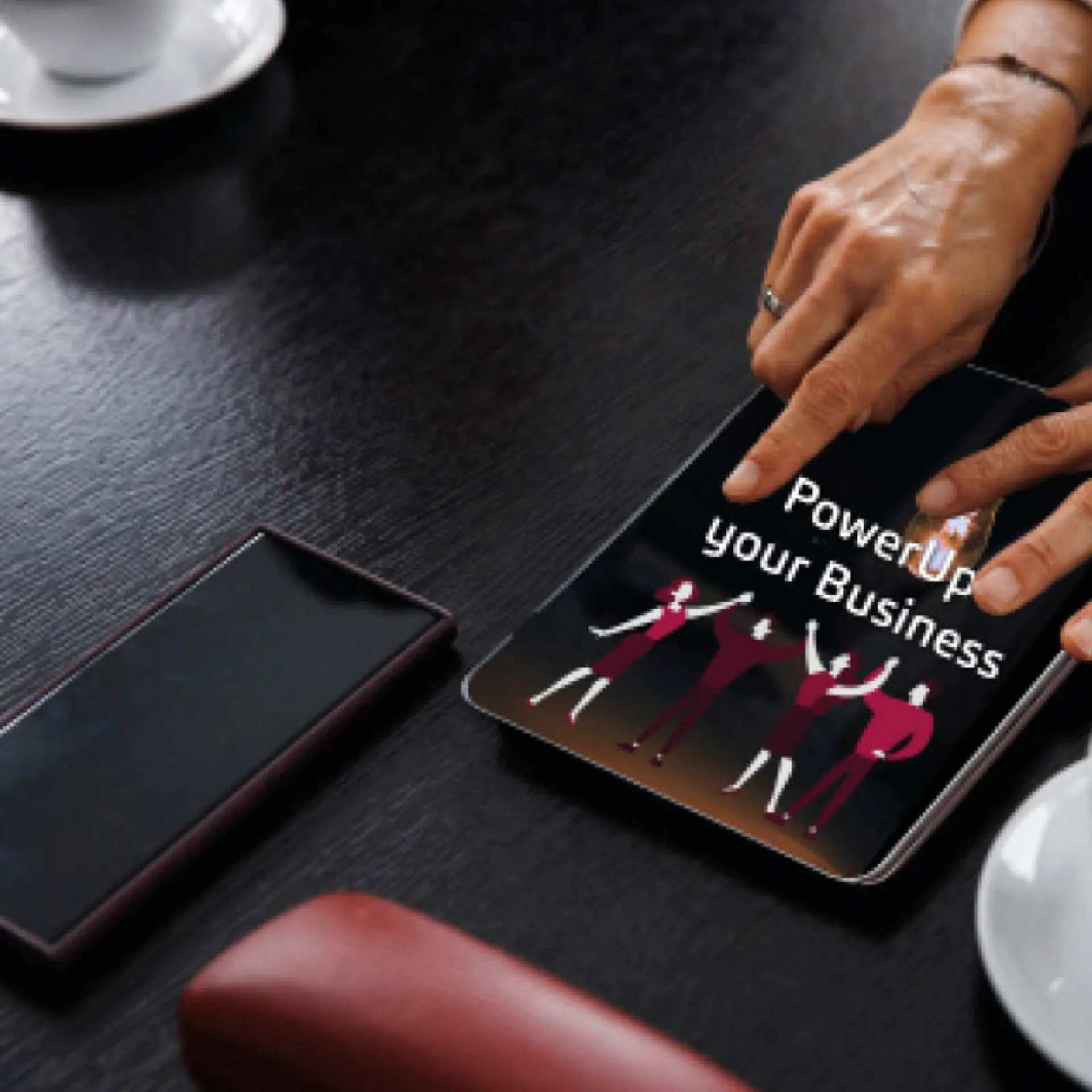 Tablet screen with “Power Up Your Business” text and illustrated team of people celebrating, hand interacting with the screen on a dark wooden table.