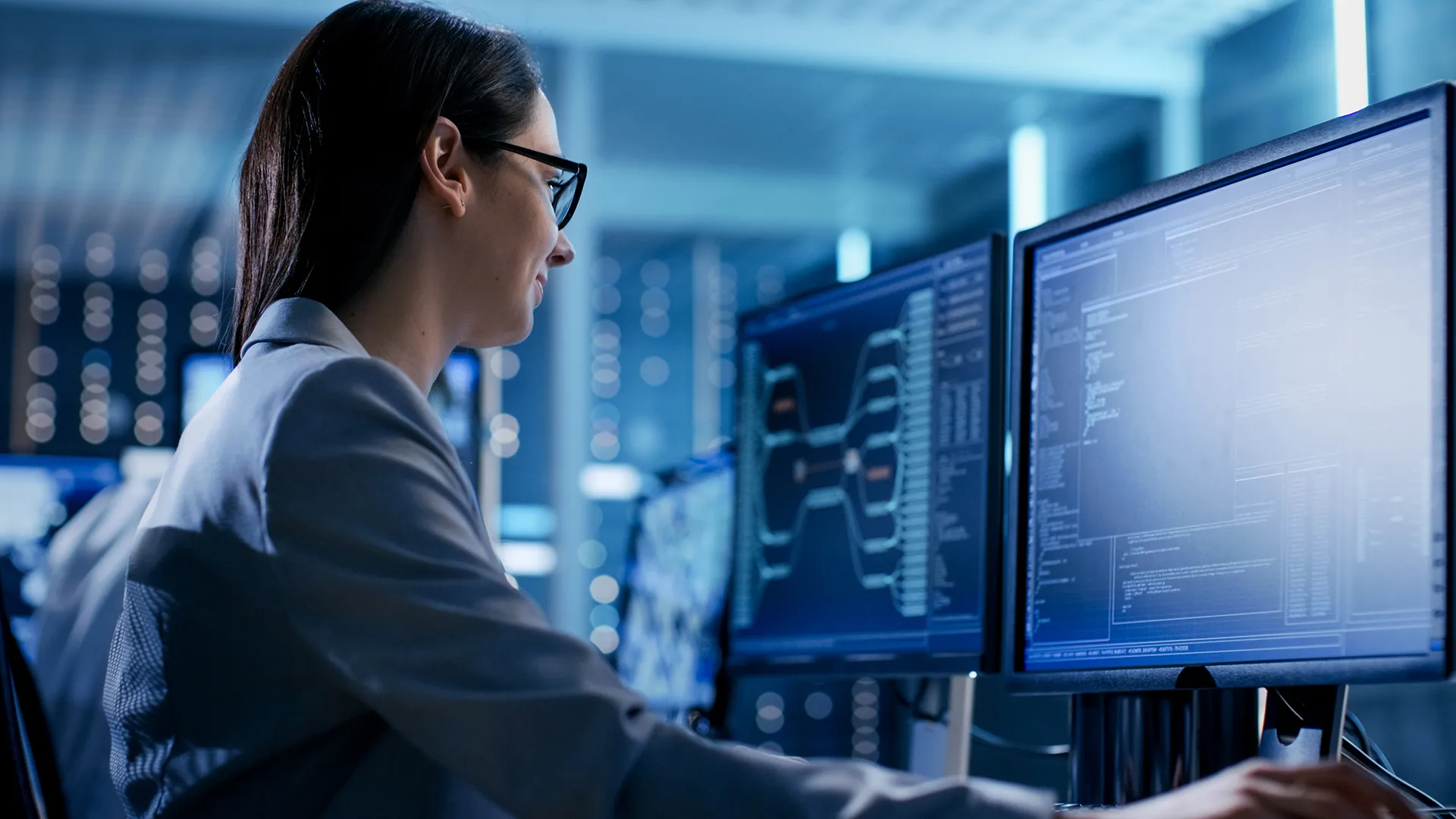Female IT specialist analyzing data on dual monitors in a secure, high-tech operations center, representing cybersecurity, system monitoring, and enterprise technology.