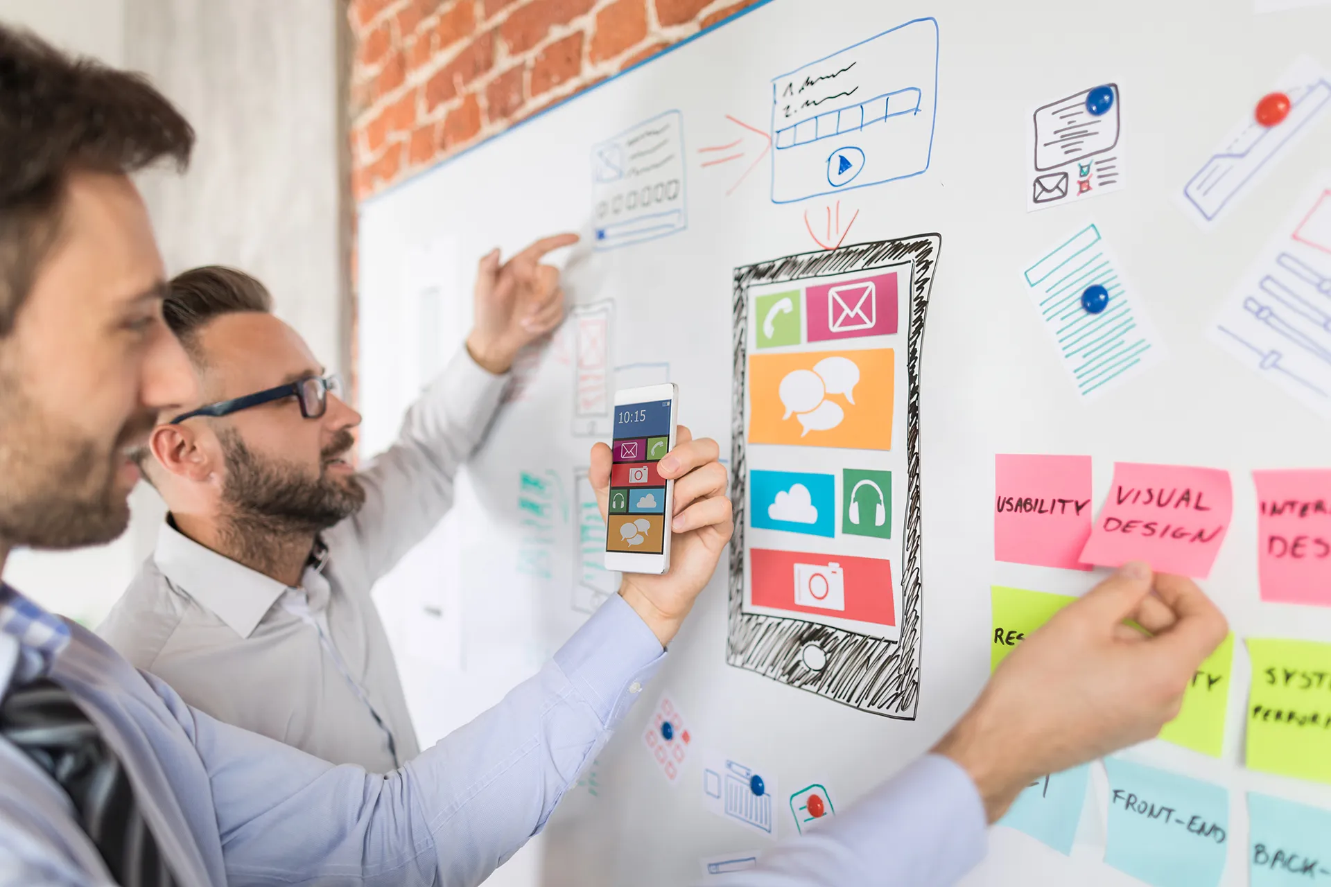 Two UX designers collaborate on a mobile app interface by sketching and organizing user interface elements on a whiteboard, highlighting usability and visual design.
