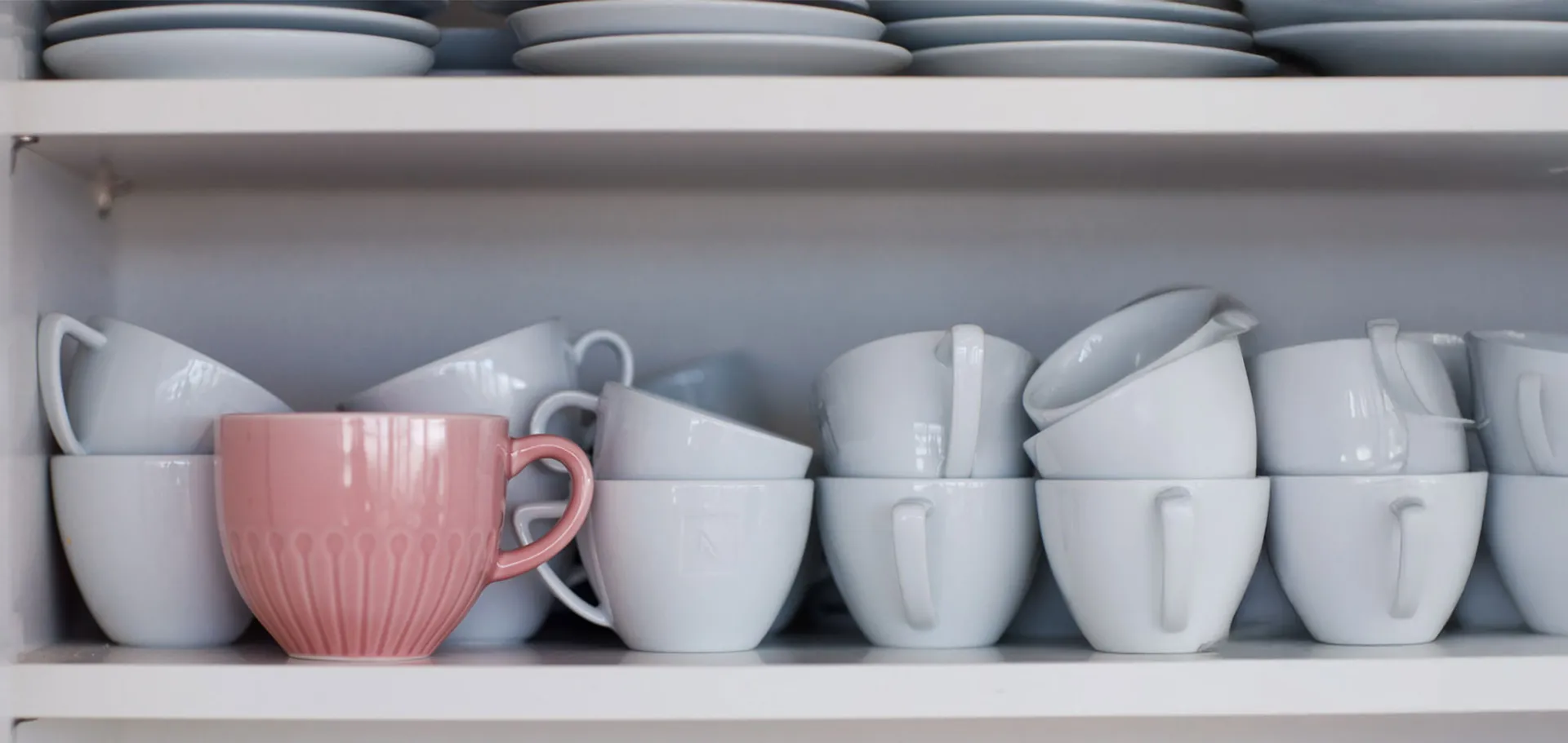  Close-up of white coffee cups stacked on a shelf with one standout pink cup, symbolizing individuality and innovation.